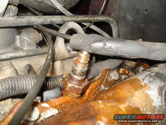 Close-up of a rusty engine component with metal lines and hoses attached