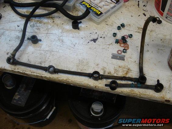 fuel rail and lines laid out on a workbench with some small parts and a razor blade
