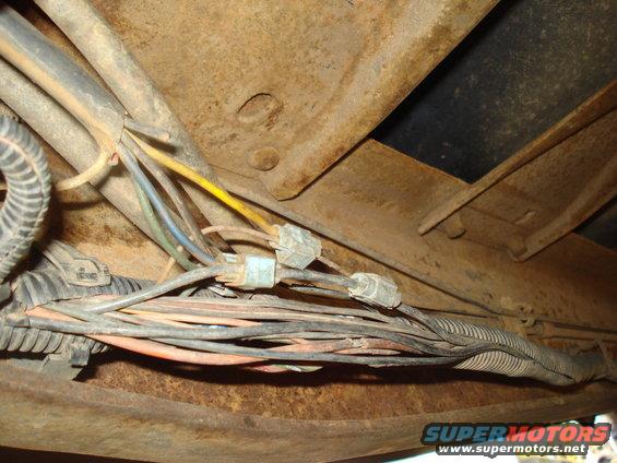 Close-up of a vehicle's rusty undercarriage showing a bundle of wires and connectors