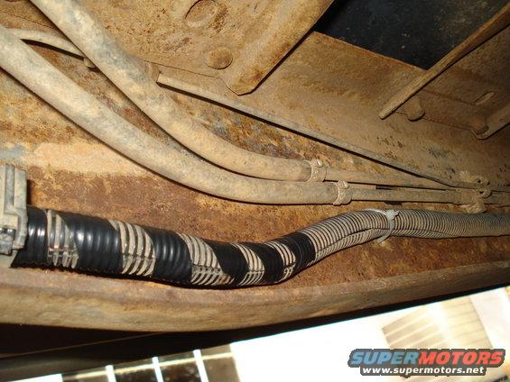 Close-up of a vehicle's underbody wiring harness with black and white tape