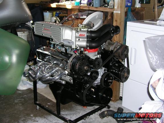V8 engine with a silver supercharger on a stand, next to a washing machine