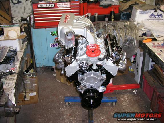 V8 engine with chrome valve covers and intake manifold, red MSD distributor cap, on an engine stand in a garage