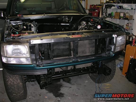 Green SUV with hood open, showing engine bay and front grille. Some wiring is visible near the front bumper