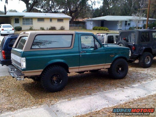 Green Ford Bronco parked next to a Jeep. It has a tan removable top