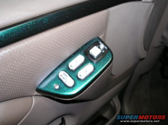 Close-up of a car's interior door panel showing power window and lock controls. The control housing is painted green with metallic flakes