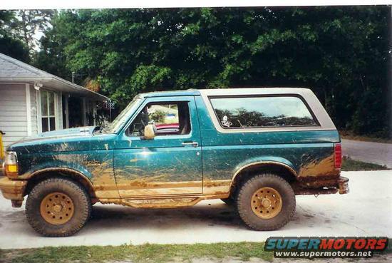 Mud-splattered teal 1992 Ford Bronco with a grey removable top, seen from the side