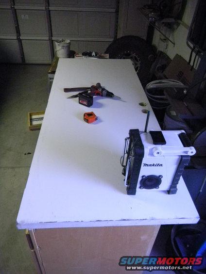 White door on a workbench with a drill, tape measure, and Makita radio. Garage background