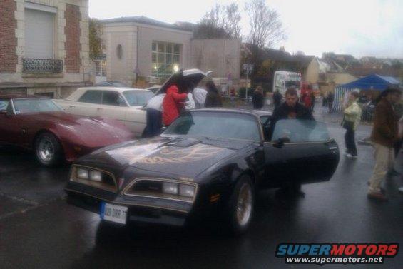 Black 1977 Pontiac Firebird Trans Am with gold decals on hood, driver's door open