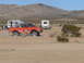 1988 Ford Bronco - An off-road vehicle races through a desert landscape, with RVs and mountains in the background.