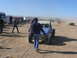 1988 Ford Bronco - A blue off-road buggy, marked with the number 990, is seen in a dusty desert environment with other vehicles and people present.