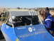 1988 Ford Bronco - A blue off-road buggy with the number 990 on its roof is seen with drivers and onlookers.
