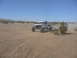 1988 Ford Bronco - A custom off-road buggy navigates a dusty desert terrain under a clear blue sky, with another vehicle visible in the distance.