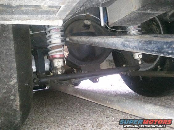 Underside view of a car's rear axle, differential, and suspension with large tires visible