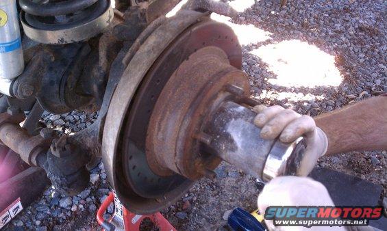 Close-up of a rusty brake rotor and hub assembly with a gloved hand holding a metal part