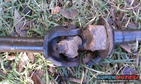 Driveshaft universal joint with rust and wear, lying on grass and leaves