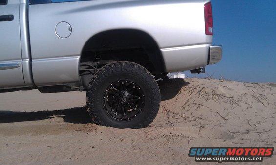 Silver pickup truck rear quarter panel and wheel on sand. 2005 Dodge 1500