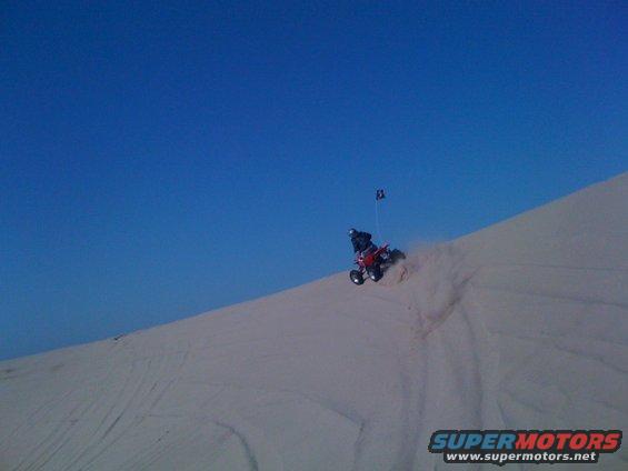 Red quad bike with rider on a sand dune, kicking up dust