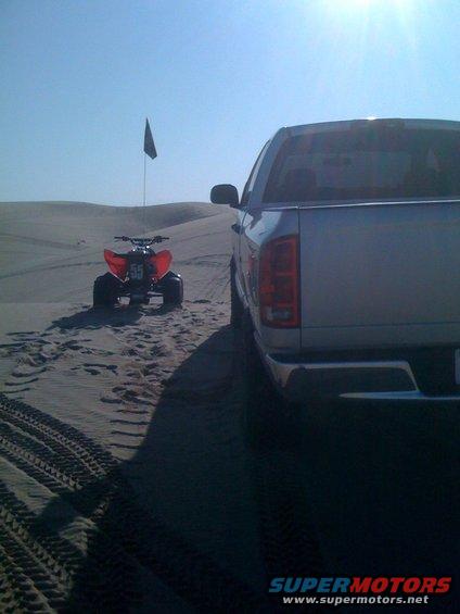 Rear view of silver 2005 Dodge 1500 pickup truck parked on sand dunes next to a red ATV