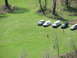 1990 Ford Bronco - Several SUVs and vans are parked on a green, grassy slope, with two individuals walking in the foreground.