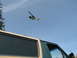 1990 Ford Bronco - A helicopter is seen in the sky above a two-tone tan and green vehicle, possibly a van or SUV.