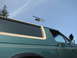 1990 Ford Bronco - A helicopter flies over a green SUV, seen from a low angle against a blue sky.