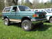1990 Ford Bronco - This green Ford Bronco is parked on a grassy field with trees in the background.