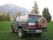 1990 Ford Bronco - A green and tan 1990 Ford Bronco is parked in a grassy field with mountains and a helicopter in the background.