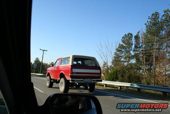 Red Ford Bronco driving on a road, seen from another car