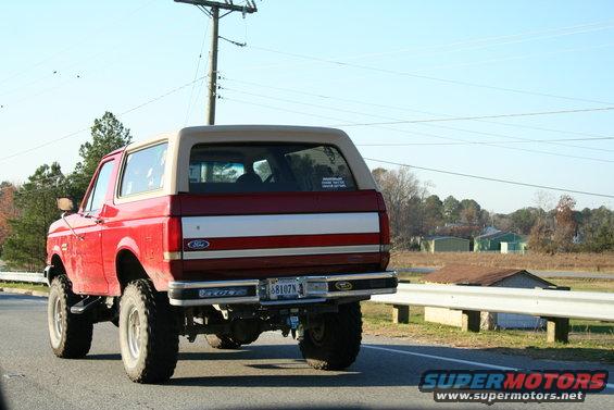 Red Ford Bronco with tan top, rear view, lifted suspension, on a road
