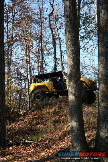 Yellow off-road SUV with a roll cage driving up a wooded hill