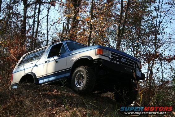 Two-tone blue and white Ford Bronco on a dirt incline, front 3/4 view