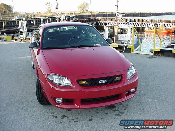 Red 2003 Ford Escort coupe front view, parked on asphalt near a dock with boats