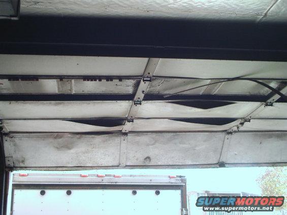 Interior of a damaged garage door with a white trailer visible below