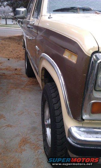 Close-up of 1980s Ford Bronco front fender, wheel, and chrome trim. Two-tone brown and tan paint