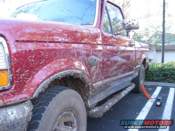 Mud-splattered red 1995 Ford F-150 pickup truck, side view, parked in a lot with an orange hose attached to the rear wheel