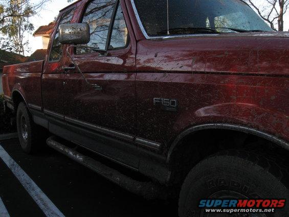 Red 1995 Ford F-150 pickup truck, side view, covered in mud, with chrome trim and running boards