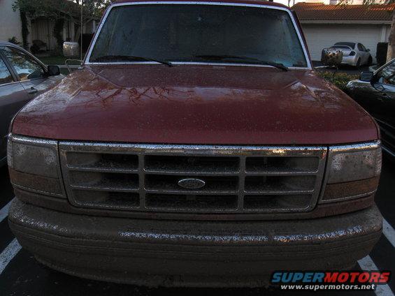 1995 Ford F-150 front view, covered in dirt and dust. Grille and bumper are heavily soiled
