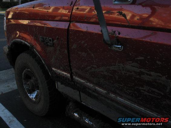 Mud-splattered red 1995 Ford F-150 side view, showing front fender, door, and tire