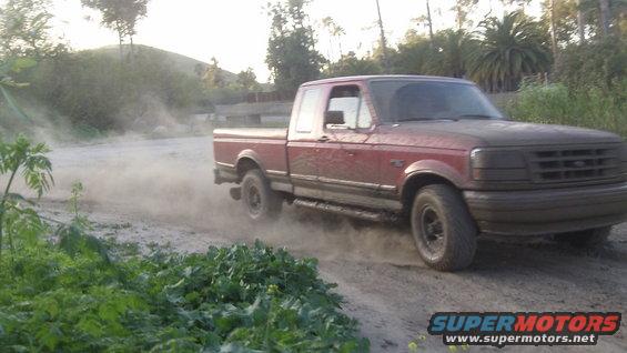 Red 1995 Ford F-150 driving on dirt road