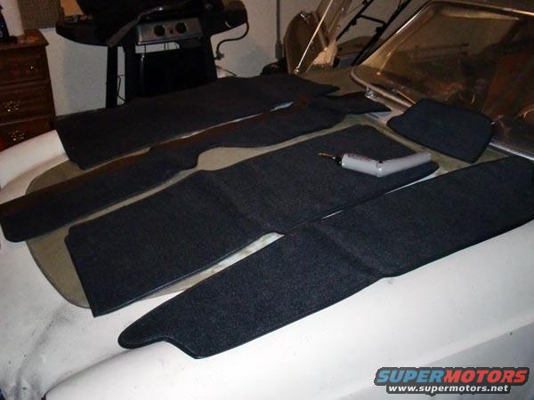 Car interior carpet pieces laid out on a car's hood. A drill is on one of the pieces