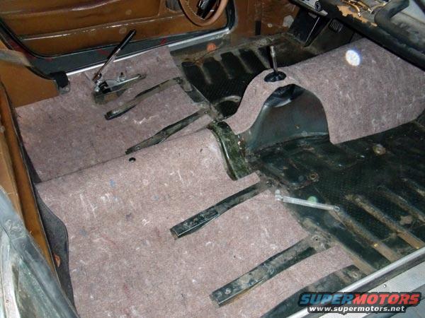 Car interior with new carpet padding installed, showing pedals and gear shifter
