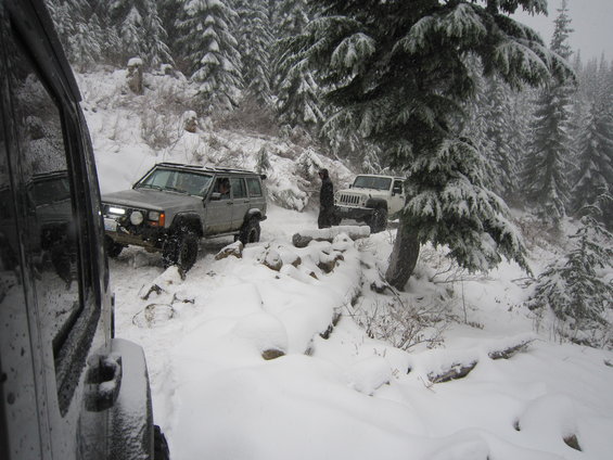 Silver Jeep Cherokee and white Jeep Wrangler driving on a snowy trail