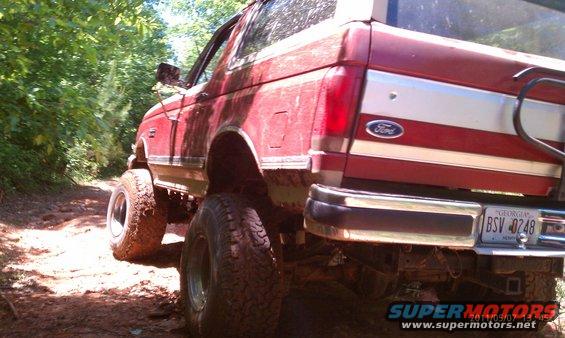 Red 1987 Ford Bronco with lifted suspension and off-road tires on a dirt path