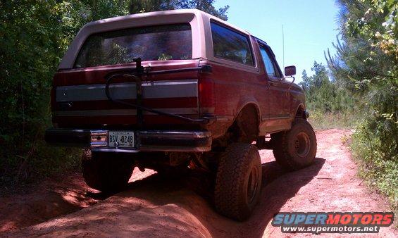 Red 1987 Ford Bronco on a dirt trail, rear view