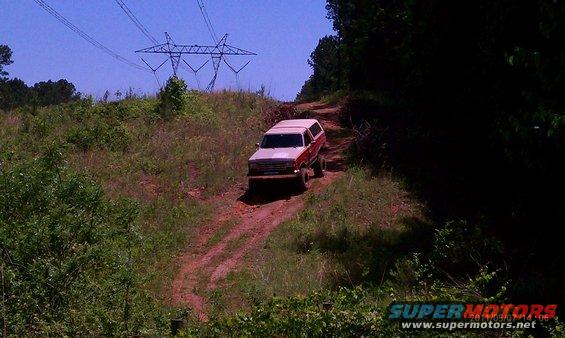 1987 Ford Bronco driving on a dirt road with power lines overhead