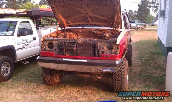 1987 Ford Bronco, hood up, engine bay exposed, parked next to a white pickup truck
