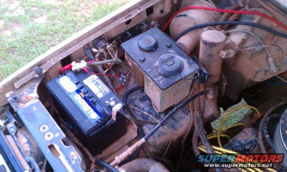 Engine bay with a black battery, brake fluid reservoir, and power steering fluid reservoir. Wires and hoses are visible