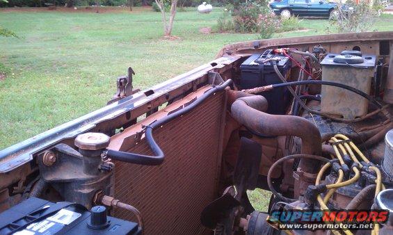 Engine bay of a brown vehicle with a rusty radiator, battery, and hoses visible