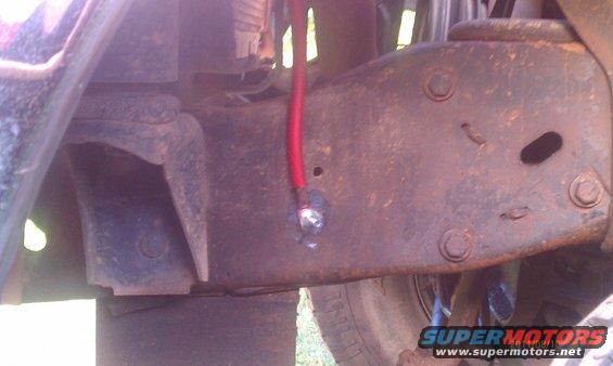 Close-up of rusted vehicle frame with a red wire attached