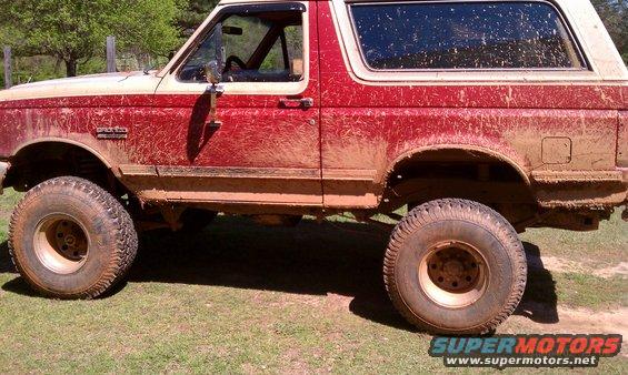 Mud-covered 1987 Ford Bronco, side view. Lifted with large tires